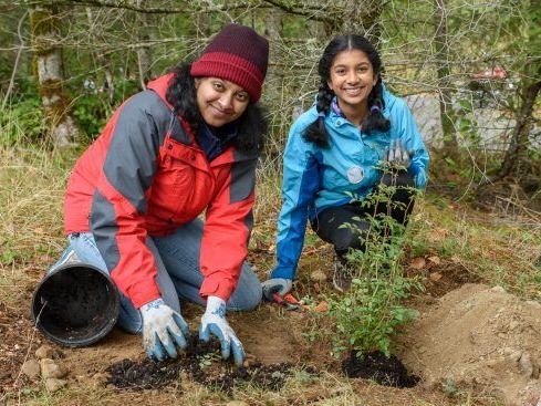 This is an image of a mother and daughter planting a tree.